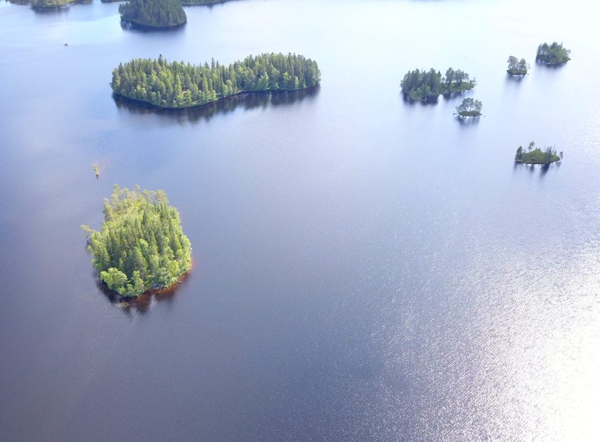 En luftbild visar en sjö med glittrande vatten. Som små prickar ligger flera skogsklädda gröna öar utspridda över den öppna ytan. En del av öarna är väldigt små.