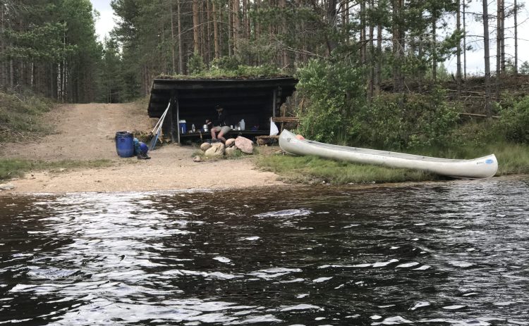 Bilden visar vindskyddet där kanotturen på Rottnan slutar. En kanot har tagits ur vattnet och packningen står redo för hämtning. En bred grusväg leder ända ner till vattnet i Skallbergssjön.
