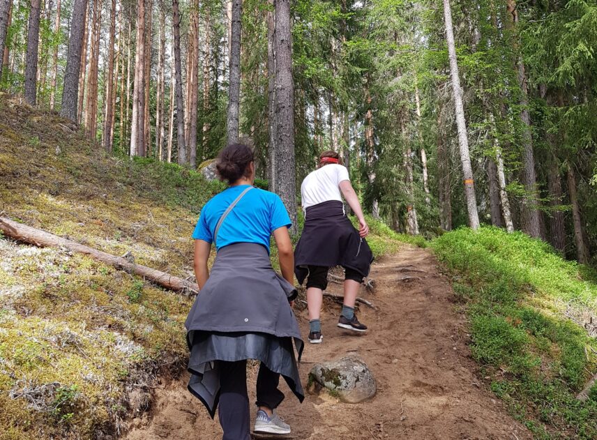 En bredare stig leder in i ett skogsparti. Två personer syns bakifrån hur de vandrar längs stigen. Det leder ganska brant uppåt. Bilden är tagen vid Femtåns vattenfall.